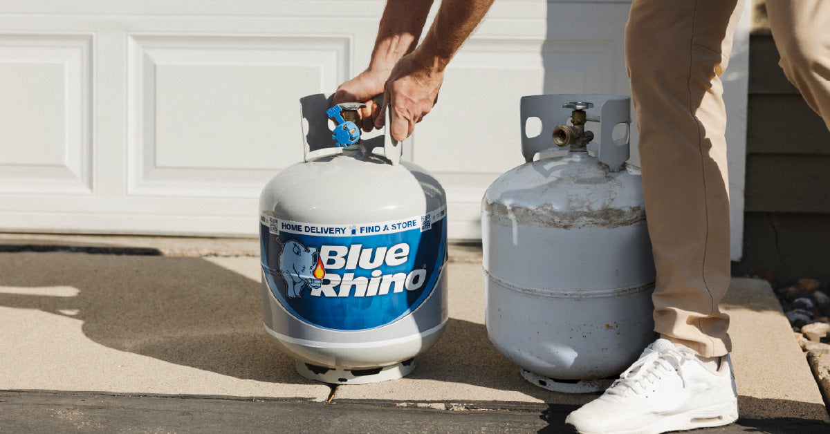 A delivery driver setting down a fresh Blue Rhino right next to an empty tank, in front of the garage door.