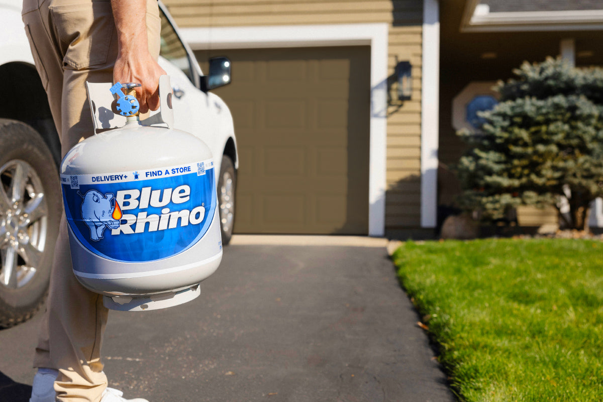Person holding a Blue Rhino propane tank in front of a house.