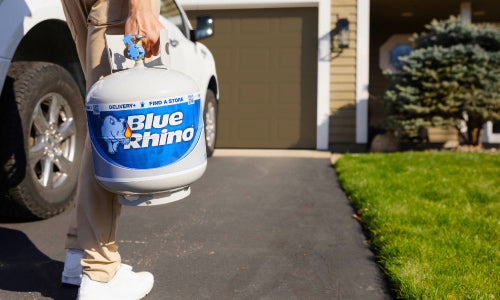Person holding a Blue Rhino propane tank in front of a house.