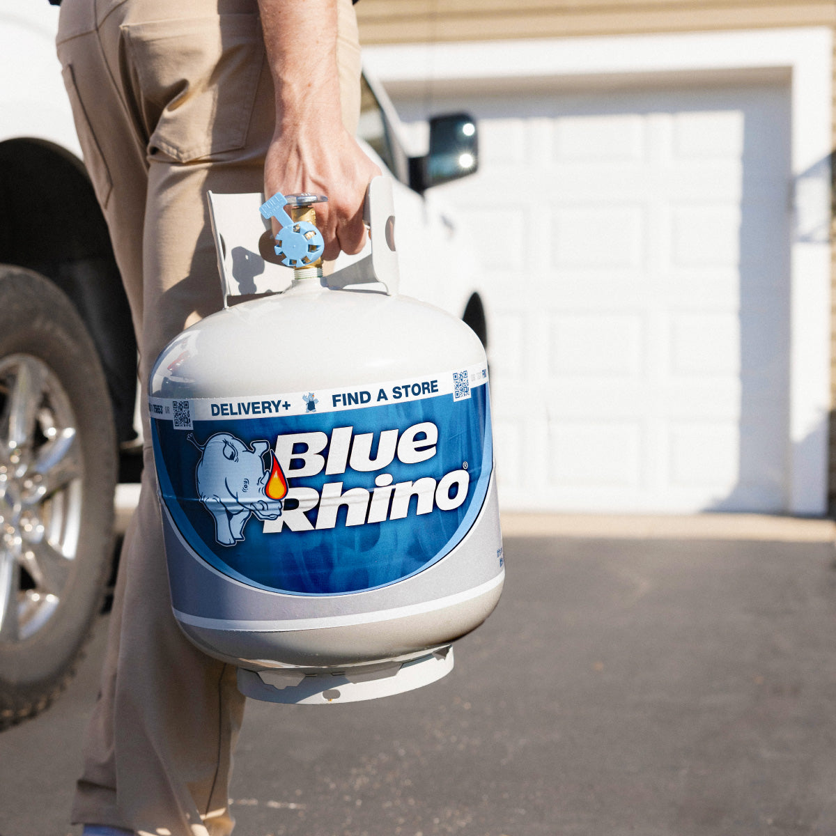 Person holding a Blue Rhino propane tank in front of a vehicle.