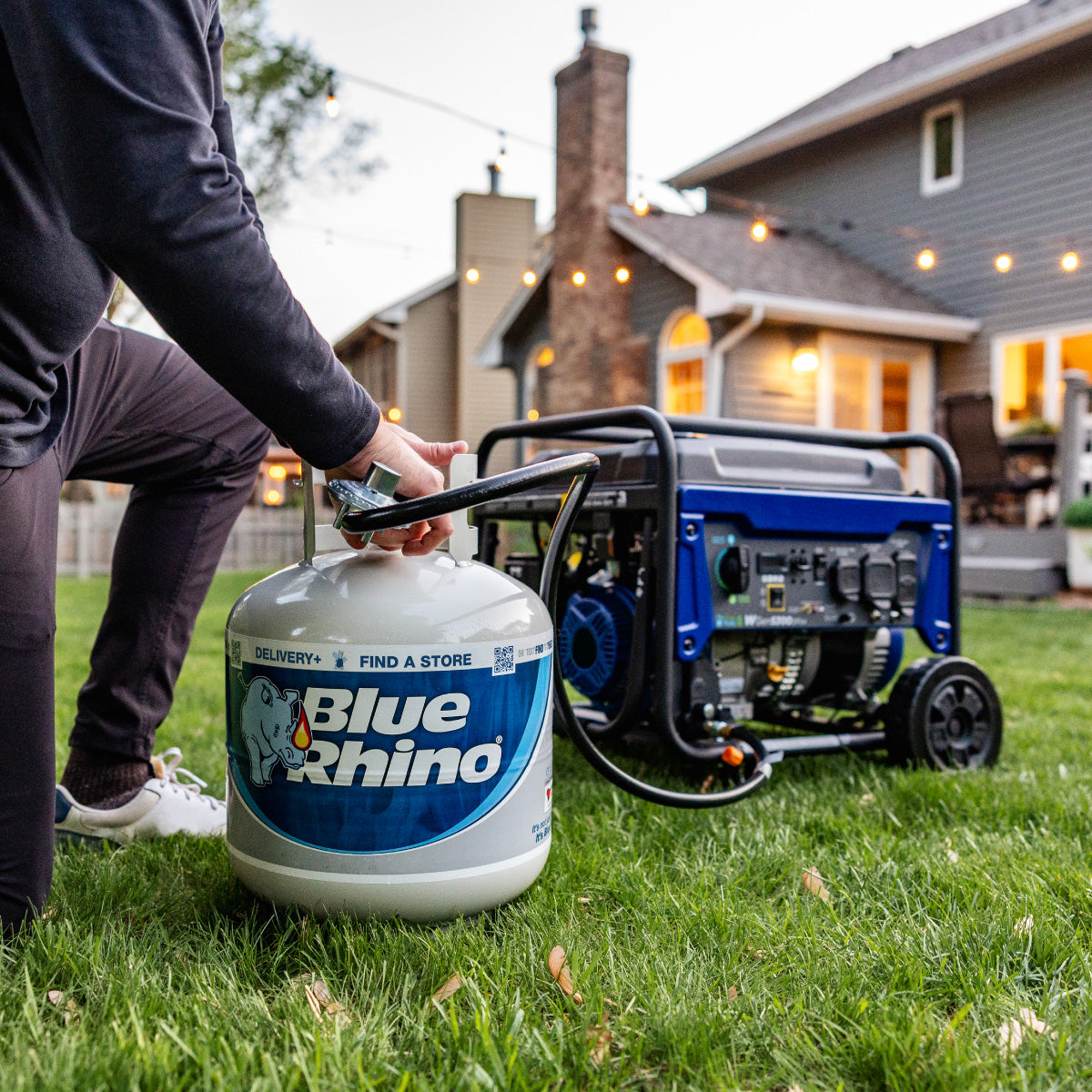 A man connecting a fresh Blue Rhino propane tank to a generator in the backyard.
