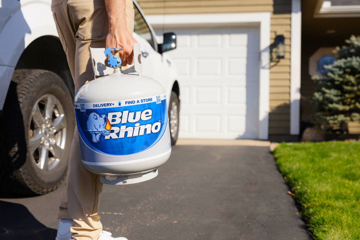 Person holding a Blue Rhino propane tank in front of a house.