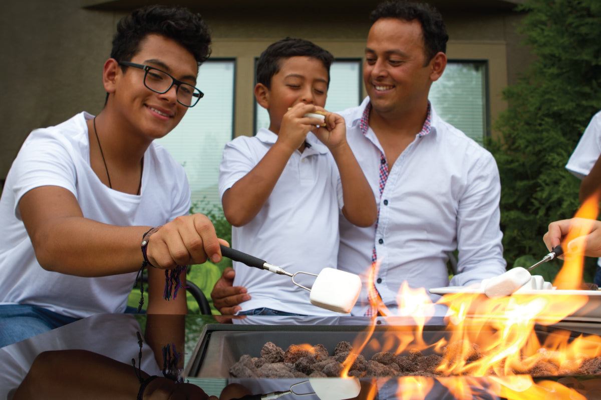Father and sons grilling marshmallows on a propane fire pit.